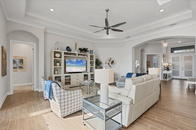 living area with arched walkways, visible vents, wood tiled floor, a raised ceiling, and crown molding