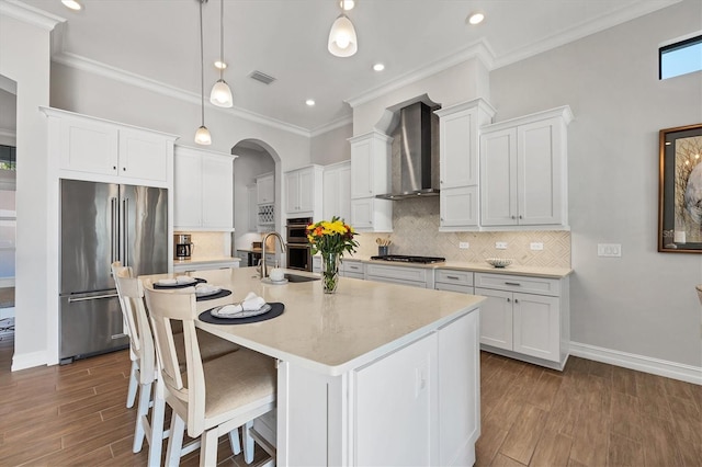 kitchen featuring visible vents, wall chimney exhaust hood, appliances with stainless steel finishes, a breakfast bar area, and a kitchen island with sink