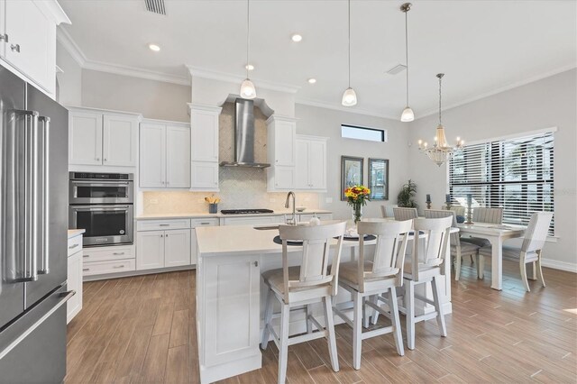 kitchen with stainless steel appliances, a sink, light wood-type flooring, wall chimney exhaust hood, and tasteful backsplash