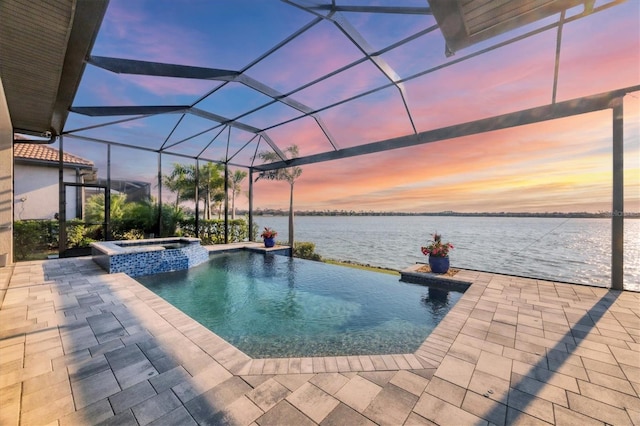 pool at dusk with a water view, a patio area, a pool with connected hot tub, and glass enclosure