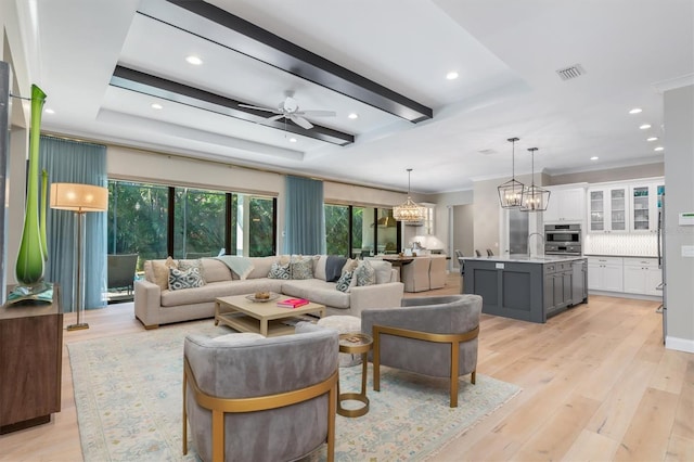 living area featuring ceiling fan with notable chandelier, beamed ceiling, visible vents, and light wood-style floors