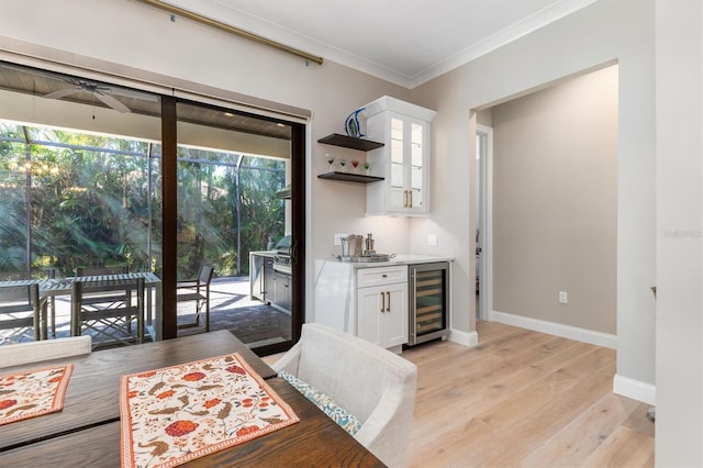 dining space featuring a dry bar, light wood-style flooring, ornamental molding, beverage cooler, and baseboards