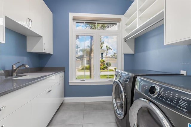 clothes washing area featuring light tile patterned flooring, a sink, baseboards, washer and dryer, and cabinet space