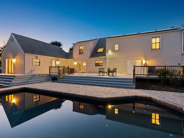 back of house at dusk with an outdoor pool and a wooden deck