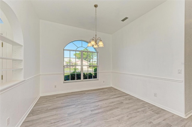 spare room featuring a chandelier, baseboards, visible vents, and light wood-style floors