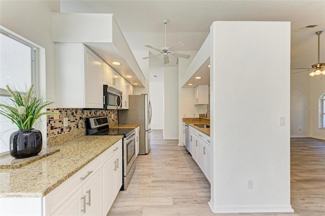 kitchen with appliances with stainless steel finishes, light wood-style floors, ceiling fan, and tasteful backsplash