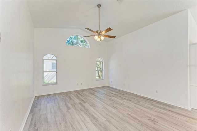 spare room featuring vaulted ceiling, light wood finished floors, a ceiling fan, and baseboards