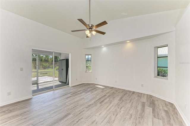 empty room with high vaulted ceiling, light wood finished floors, a ceiling fan, and baseboards