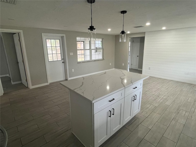 kitchen with light stone counters, decorative light fixtures, a center island, white cabinetry, and wood tiled floor