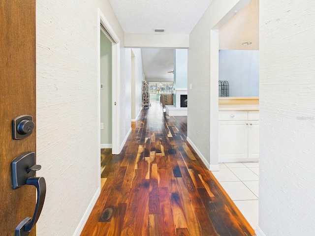 corridor with baseboards, a textured ceiling, visible vents, and wood finished floors