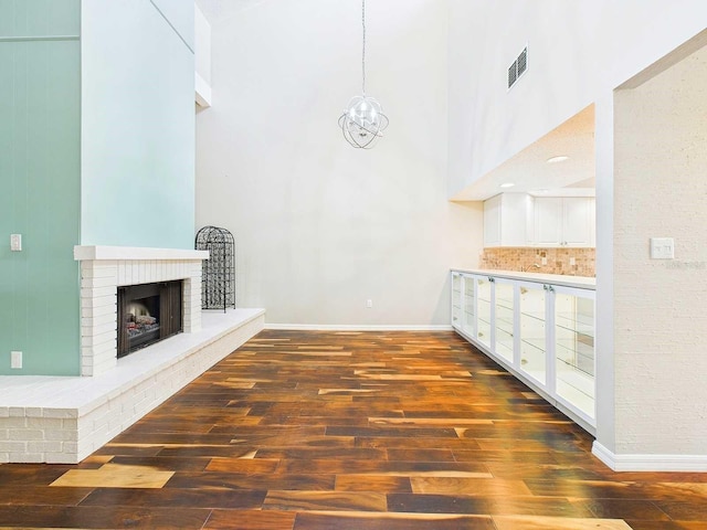 interior space with visible vents, a towering ceiling, wood finished floors, a brick fireplace, and a chandelier