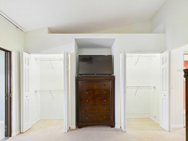 unfurnished bedroom with light carpet, baseboards, a spacious closet, vaulted ceiling, and a closet