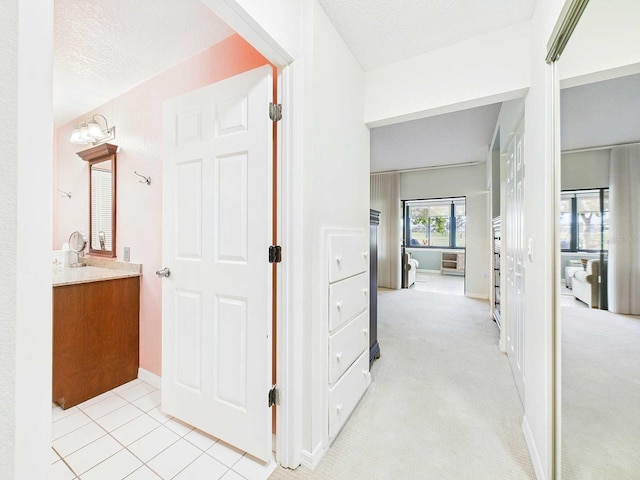 hallway featuring light carpet, a textured ceiling, and light tile patterned floors