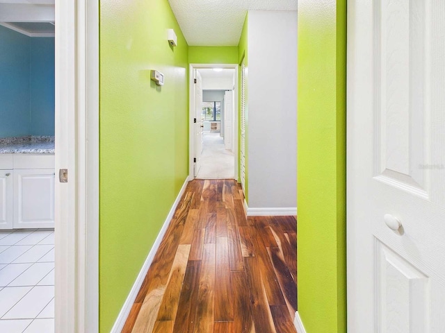 hall with a textured ceiling, light wood finished floors, and baseboards