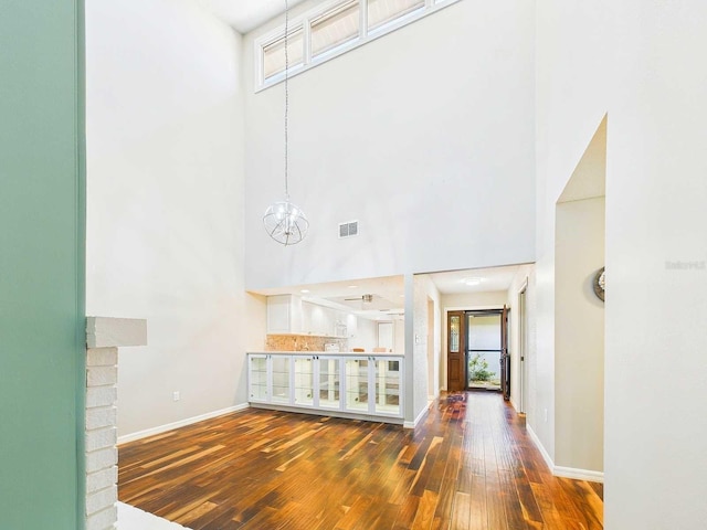 interior space featuring a chandelier, dark wood-type flooring, a high ceiling, visible vents, and baseboards