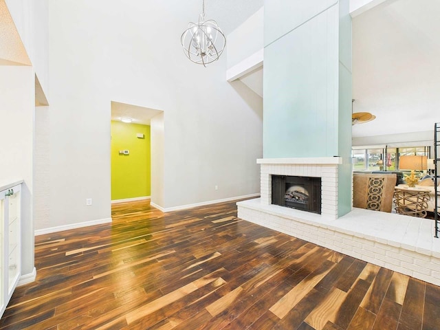 unfurnished living room with an inviting chandelier, a fireplace, baseboards, and wood finished floors