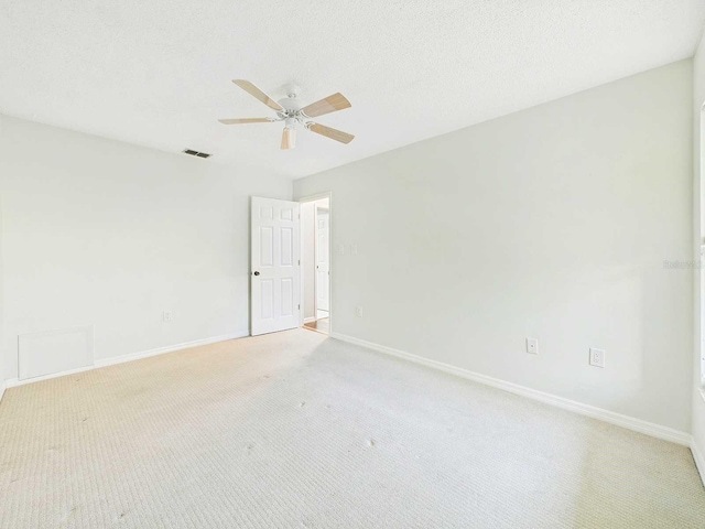 spare room with a textured ceiling, ceiling fan, light colored carpet, visible vents, and baseboards