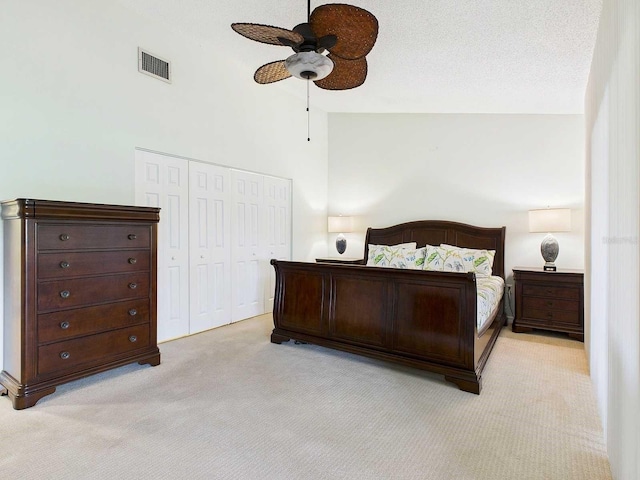 bedroom featuring ceiling fan, a textured ceiling, light carpet, visible vents, and a closet