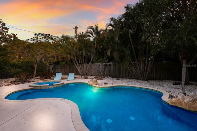 pool at dusk with a patio, a pool with connected hot tub, and a fenced backyard