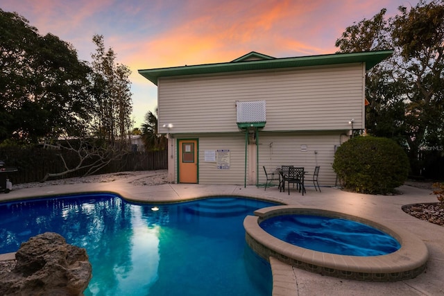 pool at dusk featuring a patio area, fence, and a pool with connected hot tub