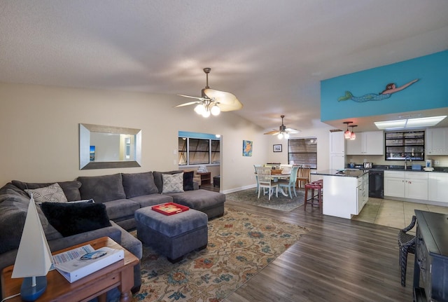 living area with a ceiling fan, vaulted ceiling, light wood-style floors, and baseboards