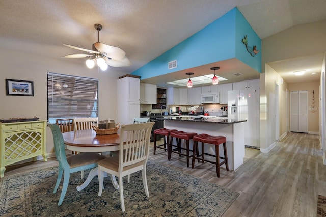 dining room featuring light wood-style floors, a ceiling fan, and vaulted ceiling