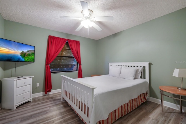 bedroom featuring a ceiling fan, wood finished floors, baseboards, and a textured ceiling