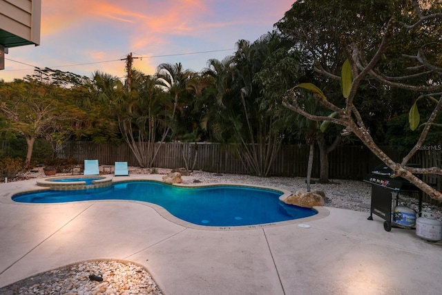 pool at dusk featuring a patio area, a pool with connected hot tub, and a fenced backyard