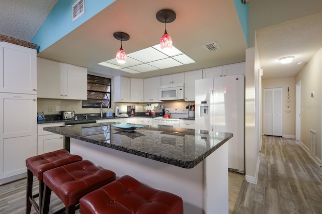 kitchen with visible vents, white cabinets, white appliances, and a sink