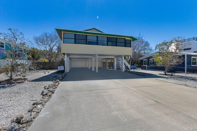 view of front of house with stairs, driveway, fence, a carport, and a sunroom