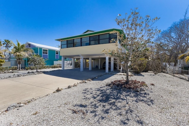 view of front facade featuring a sunroom, fence, concrete driveway, and a carport