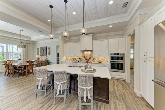 kitchen featuring a raised ceiling, light wood-style flooring, appliances with stainless steel finishes, backsplash, and a sink