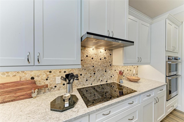 kitchen with light stone counters, tasteful backsplash, exhaust hood, stainless steel double oven, and black electric cooktop