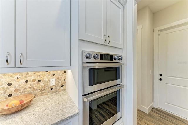 kitchen featuring white cabinets, decorative backsplash, stainless steel double oven, and wood finished floors