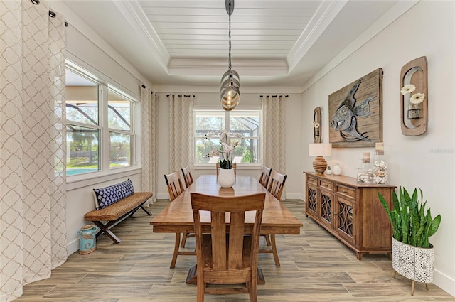 dining room with light wood-type flooring, a raised ceiling, crown molding, and baseboards