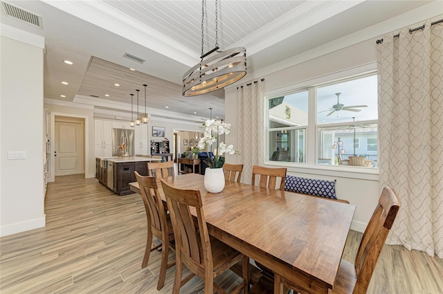 dining area with light wood-type flooring, a tray ceiling, visible vents, and ornamental molding