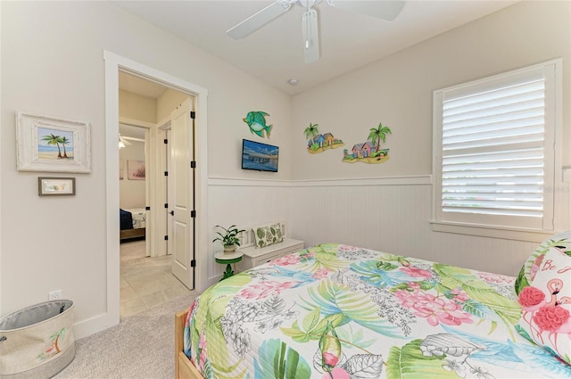 bedroom with a ceiling fan, light colored carpet, and wainscoting