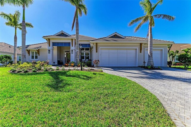 view of front of home with an attached garage, a tiled roof, decorative driveway, stucco siding, and a front yard