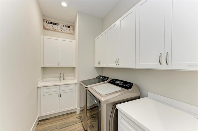 laundry area featuring light wood-style flooring, a sink, baseboards, cabinet space, and washing machine and clothes dryer