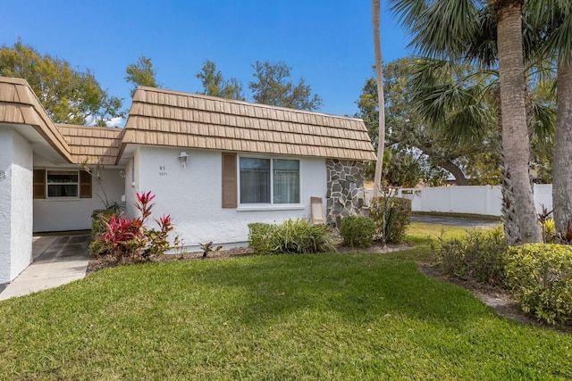 back of property featuring stucco siding, fence, mansard roof, and a yard