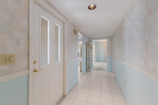 corridor with light tile patterned floors, a textured ceiling, and a notable chandelier