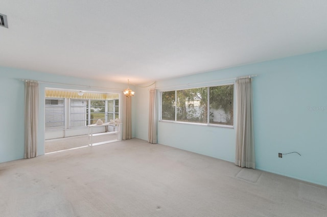 empty room featuring carpet floors, visible vents, and an inviting chandelier