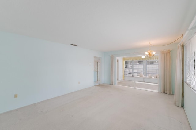 empty room featuring light carpet, a notable chandelier, and visible vents