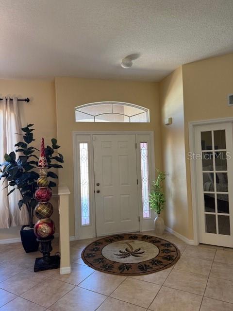 entryway with light tile patterned floors, baseboards, and a textured ceiling