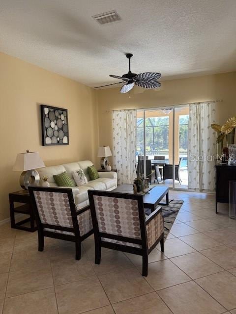 living area featuring light tile patterned floors, visible vents, a ceiling fan, a textured ceiling, and baseboards