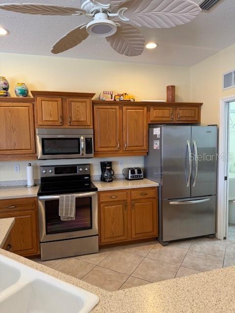 kitchen with stainless steel appliances, light countertops, brown cabinetry, and visible vents