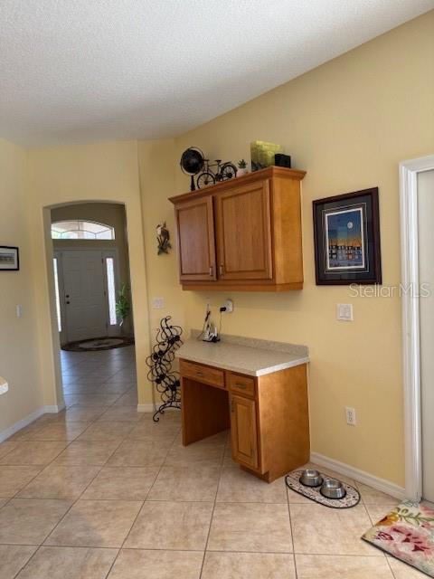 kitchen with brown cabinetry, light tile patterned floors, baseboards, and light countertops