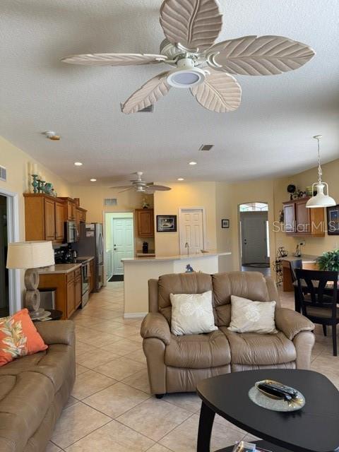 living room with a ceiling fan, visible vents, a textured ceiling, and light tile patterned floors