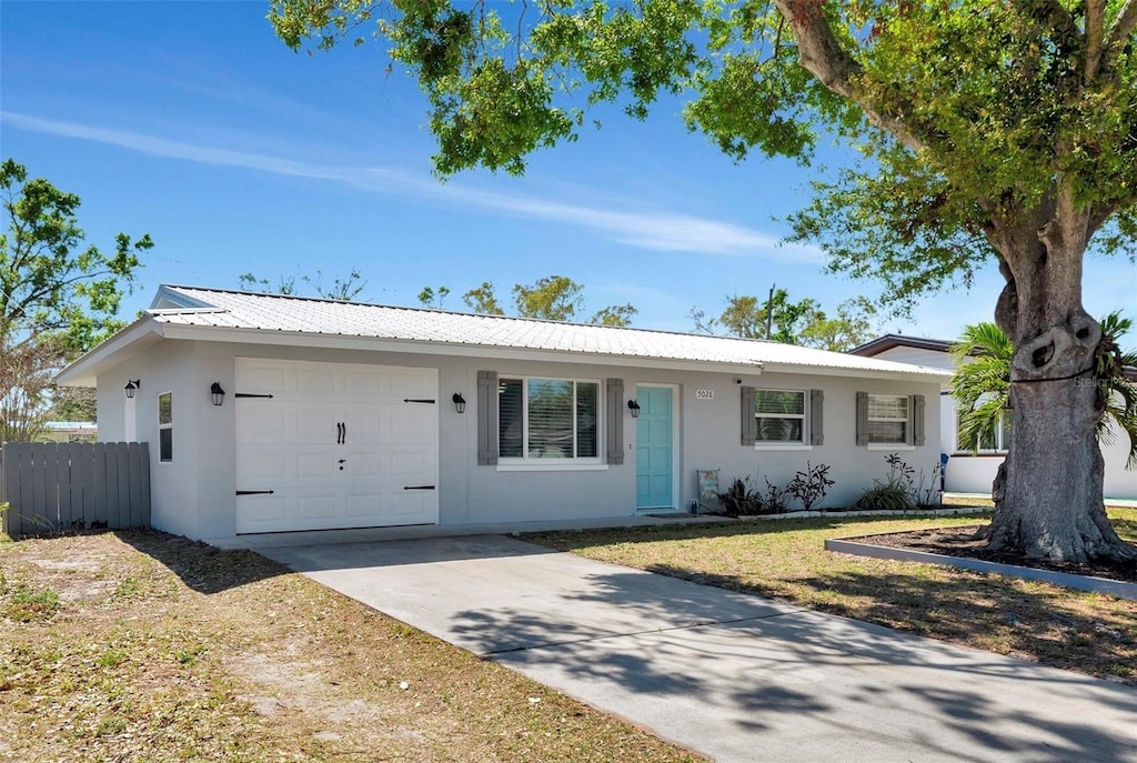 ranch-style home featuring metal roof, an attached garage, fence, and stucco siding