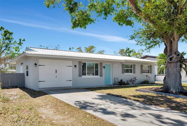 ranch-style home featuring metal roof, an attached garage, fence, and stucco siding